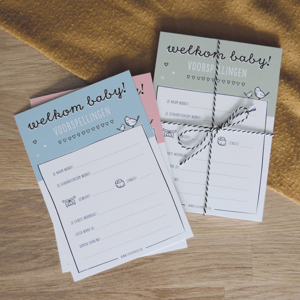 Sfeerfoto op tafel met verschillende varianten van de babyshower invulkaarten in het groen, roze en blauw.
