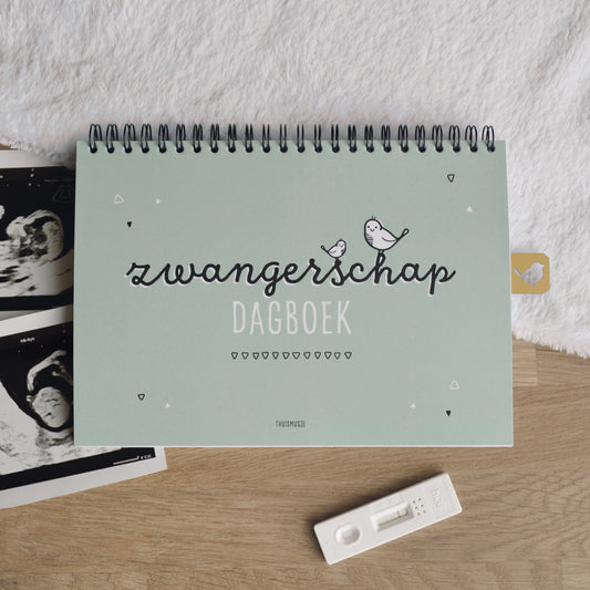 Sfeerbeeld vooraanzicht zwangerschap dagboek, op houten tafel met zacht kleedje, echofoto en zwangerschapstest.