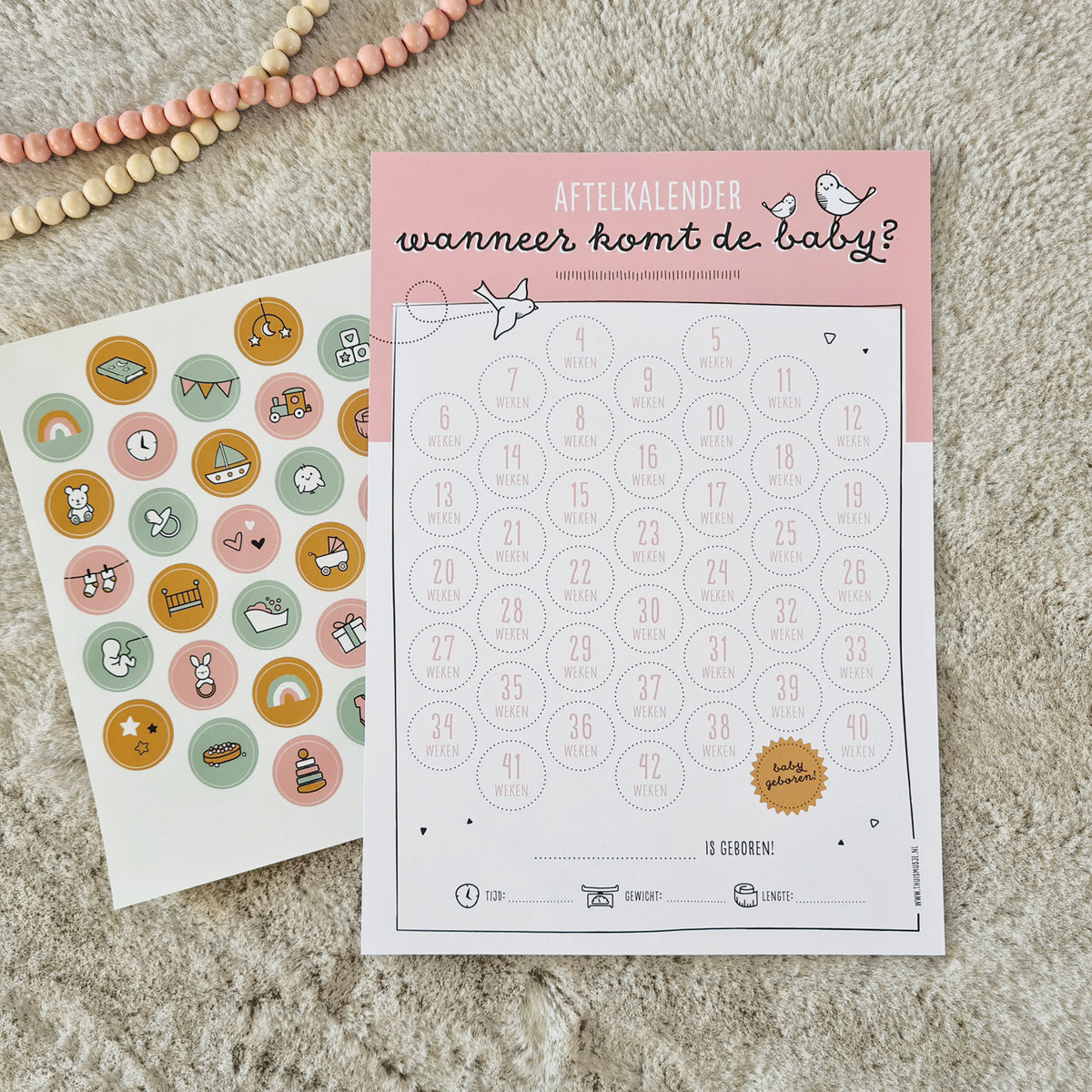 Sfeerfoto roze aftelkalender zwanger op zacht kleed met kralenketting en vrolijk stickervel