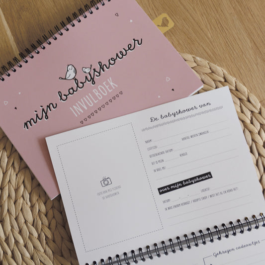 Sfeerbeeld van het babyshower invulboek met een inkijkje in de binnenkant. Titel van het blad is de babyshower van, met daaronder leuke vragen en ruimte voor een foto. 