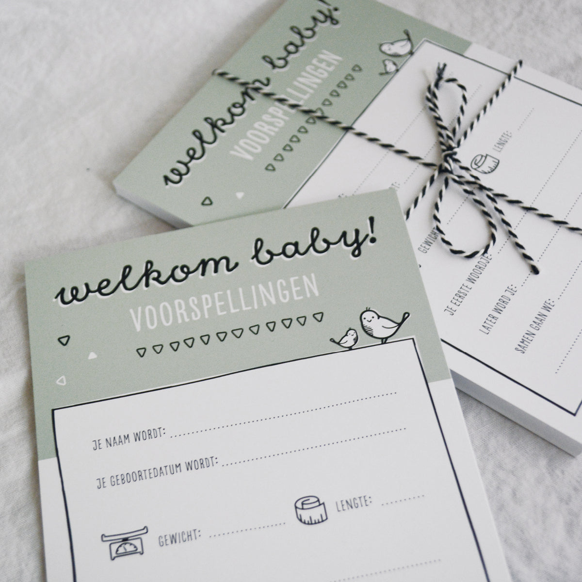 Sfeerbeeld babyshower invulkaarten met zwart wit bakkerstouwtje om een stapeltje kaarten heen gestrikt als mooie bundel. 