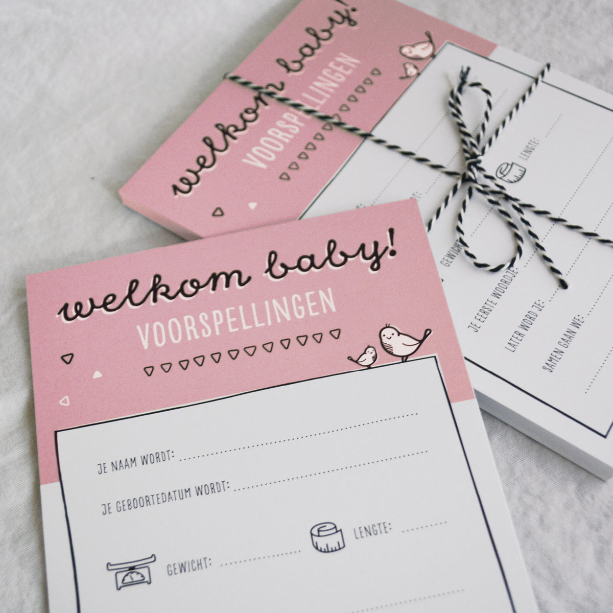 Sfeerbeeld babyshower invulkaarten met zwart wit bakkerstouwtje om een stapeltje kaarten heen gestrikt als mooie bundel. 