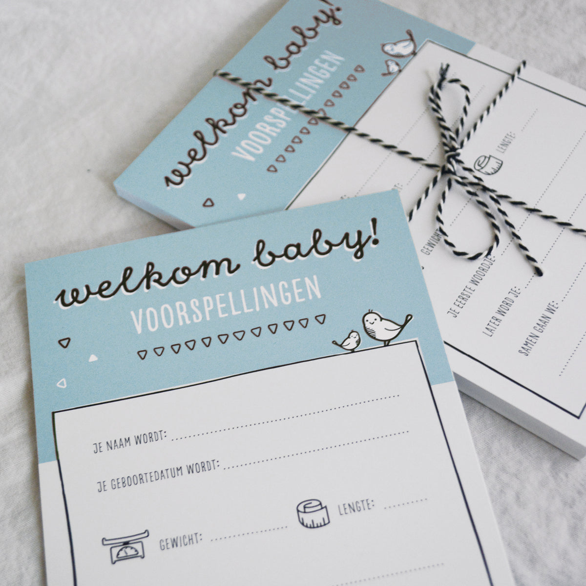 Sfeerbeeld babyshower invulkaarten met zwart wit bakkerstouwtje om een stapeltje kaarten heen gestrikt als mooie bundel. 