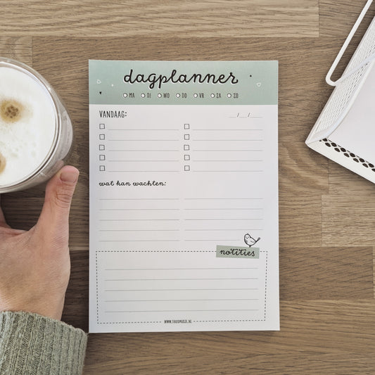 Sfeerbeeld van dagplanner op tafel met kop koffie in de hand. 