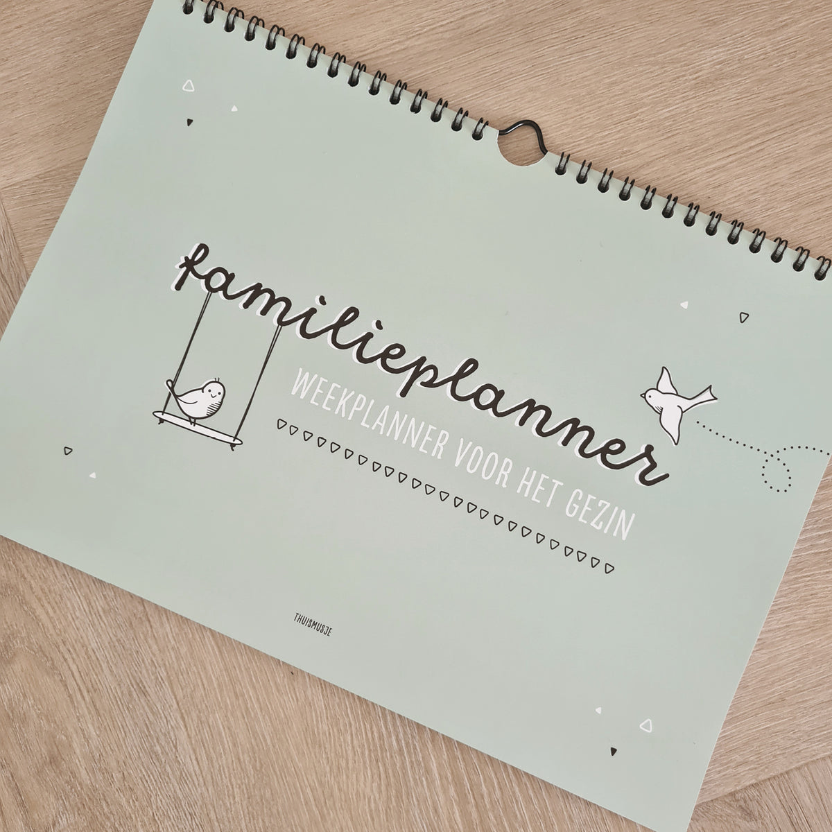 Sfeerfoto van familieplanner op houten tafel. Extra tekst welke op voorzijde staat is: weekplanner voor het gezin. 