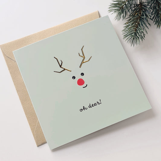 kerstkaart met rendiertje met goudfolie erop en de tekst: oh deer! weergegeven met kraft envelop en een dennentak