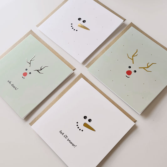Afbeelding van 4 verschillende kerstkaarten met goudfolie, liggend op kraft enveloppen.