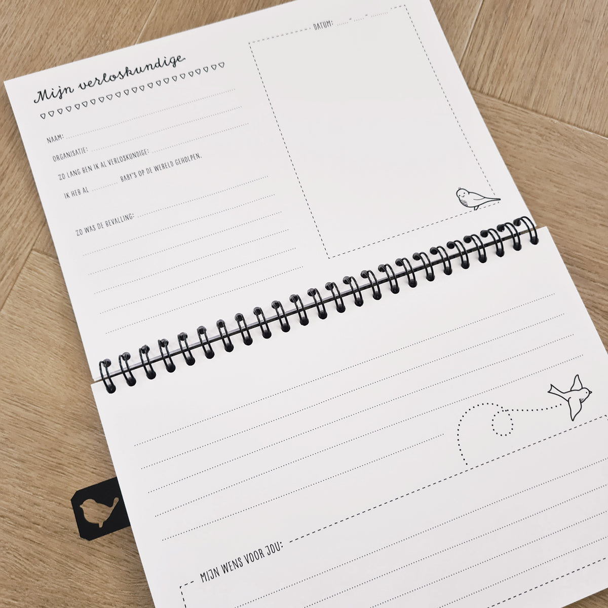 Detailfoto van binnenzijde boek met schrijfruimte voor de verloskundige. Ruimte voor een foto en voldoende schrijfruimte. Kraambezoekboek ligt op houten ondergrond. 