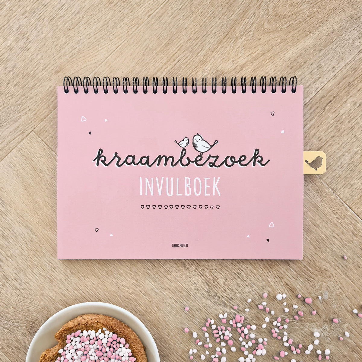 Sfeerbeeld voorzijde kraambezoekboek op houten ondergrond met een bordje beschuit met roze muisjes. 