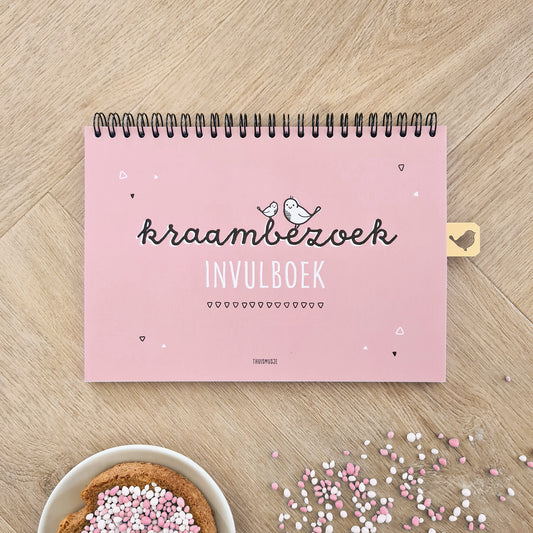 Sfeerbeeld voorzijde kraambezoekboek op houten ondergrond met een bordje beschuit met roze muisjes. 