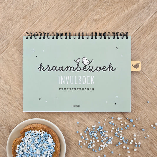 Sfeerbeeld voorzijde kraambezoekboek op houten ondergrond met een bordje beschuit met blauwe muisjes. 