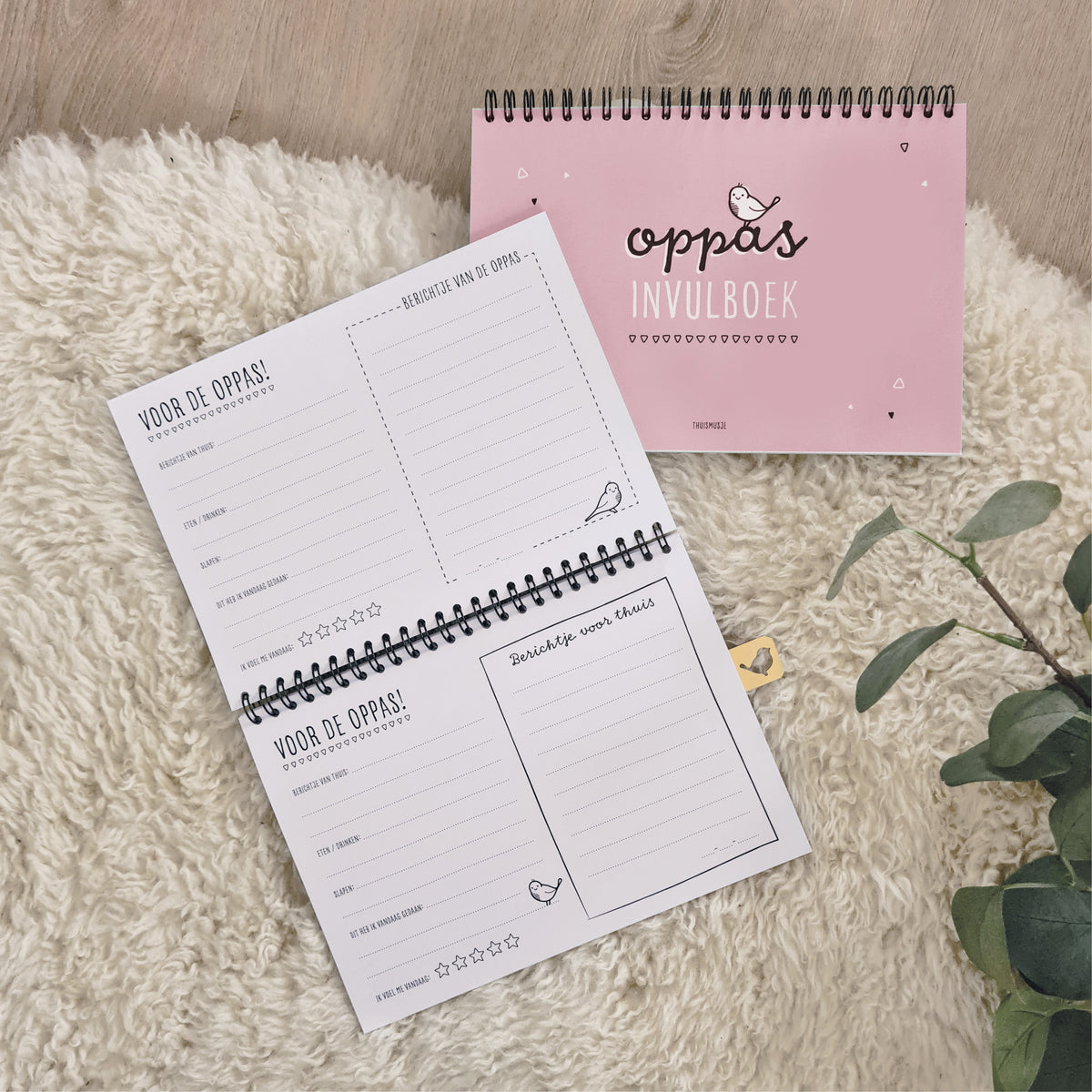 Sfeerbeeld roze oppasboekje op schapenkleed met opengeslagen invulboek erbij. invulbare pagina's te zien voor de oppas. 