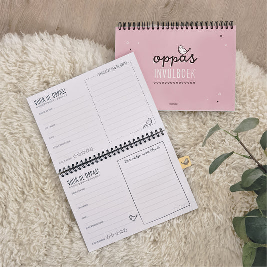 Sfeerbeeld roze oppasboekje op schapenkleed met opengeslagen invulboek erbij. invulbare pagina's te zien voor de oppas. 