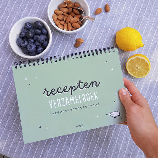 sfeerbeeld van receptenboek in de hand met op de achtergrond verse producten als bosbessen, amandelen en citroen.