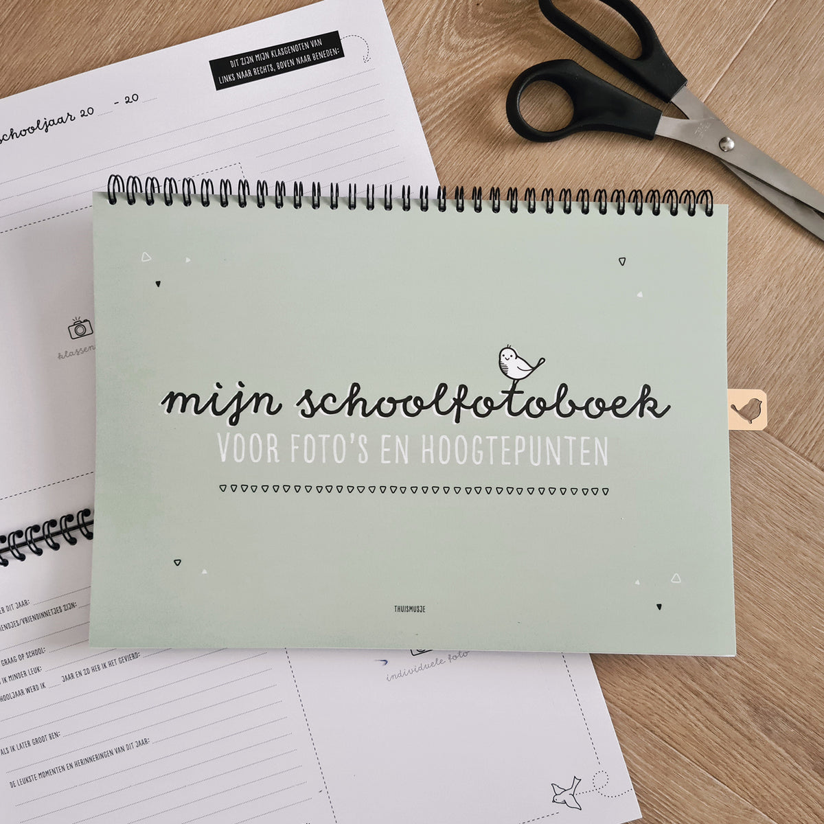 Sfeerbeeld van groen schoolfotoboek op houten tafel met schaar en opengeslagen schoolfotoboek. 