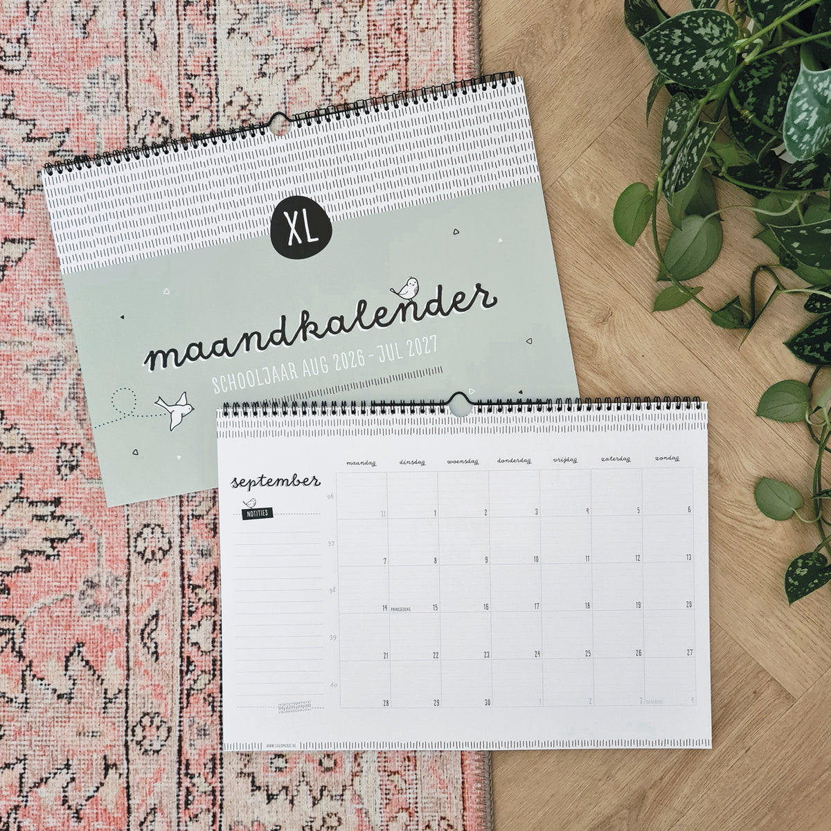 Sfeerbeeld van gesloten en opengeslagen groene maandkalender op de maand september. Liggend op een roze vloerkleed met plant ernaast. 