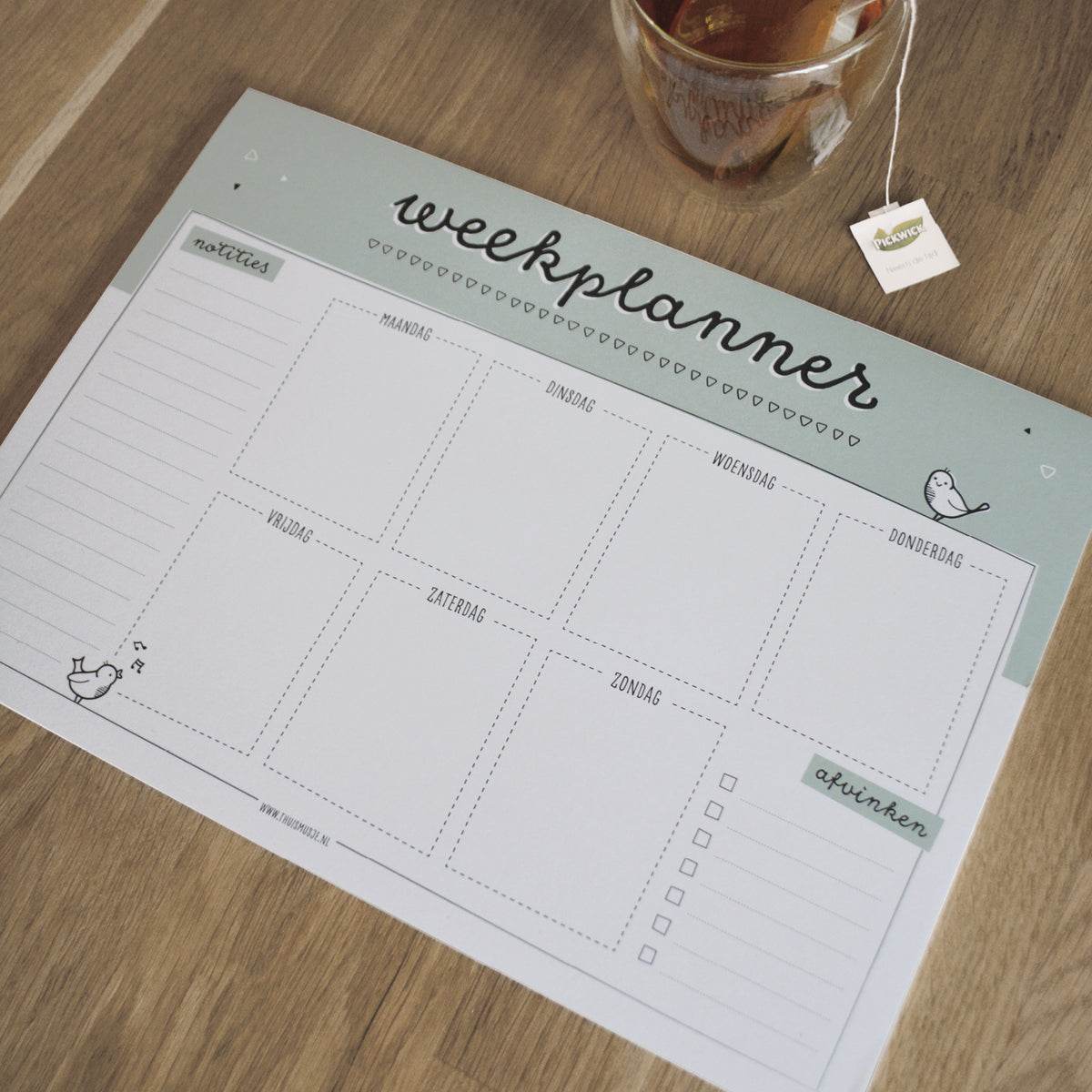 A4 weekplanner op houten tafel met kopje thee ernaast ter indicatie van grootte.