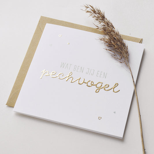 Wenskaart met goudfolie met de tekst wat ben jij een pechvogel. Weergegeven met kraft envelop