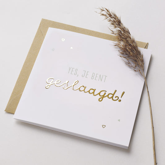 Wenskaart met goudfolie met de tekst yes, je bent geslaagd! Weergegeven met kraft envelop