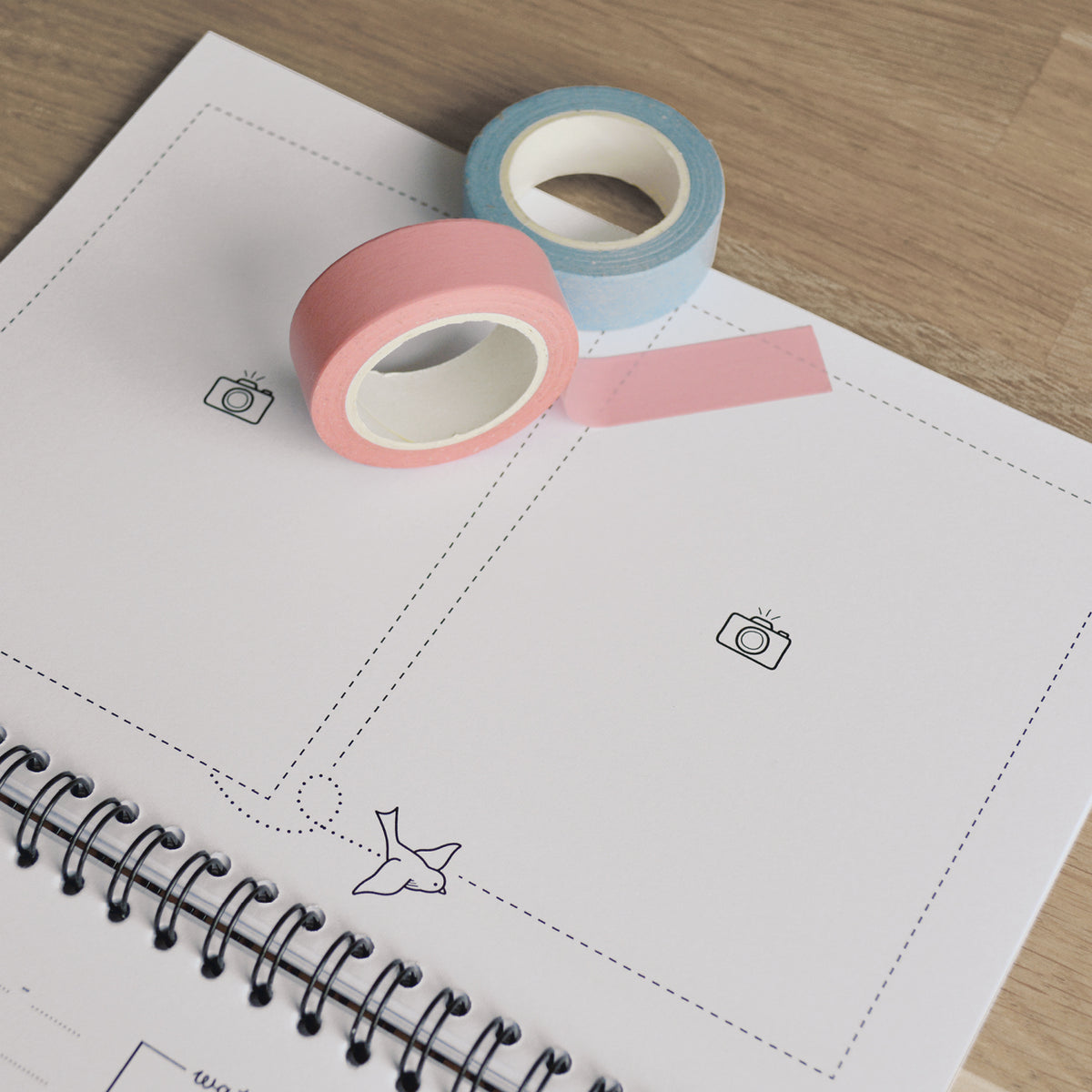 Close up van pagina waarop foto's ingeplakt kunnen worden. Sfeerbeeld van opengeslagen boek op houten tafel met twee rolletjes washitape in roze en blauw. 
